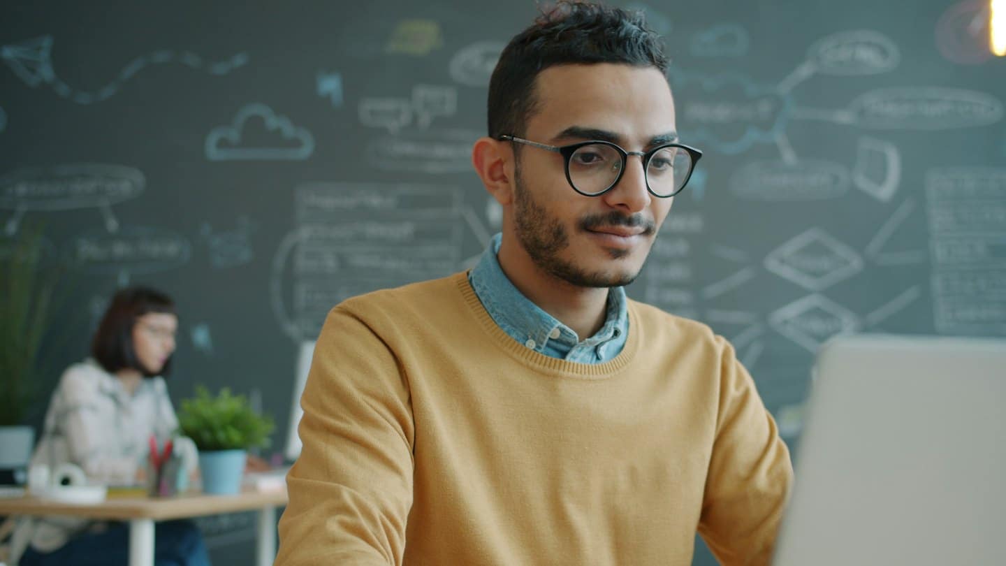 Mann mit Brille arbeitet am Laptop in einem modernen Büro.