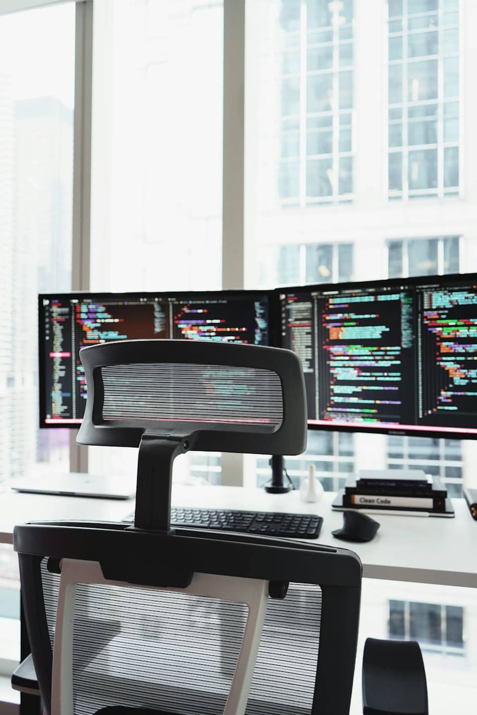 Zwei Computermonitore mit Code auf einem weißen Schreibtisch.