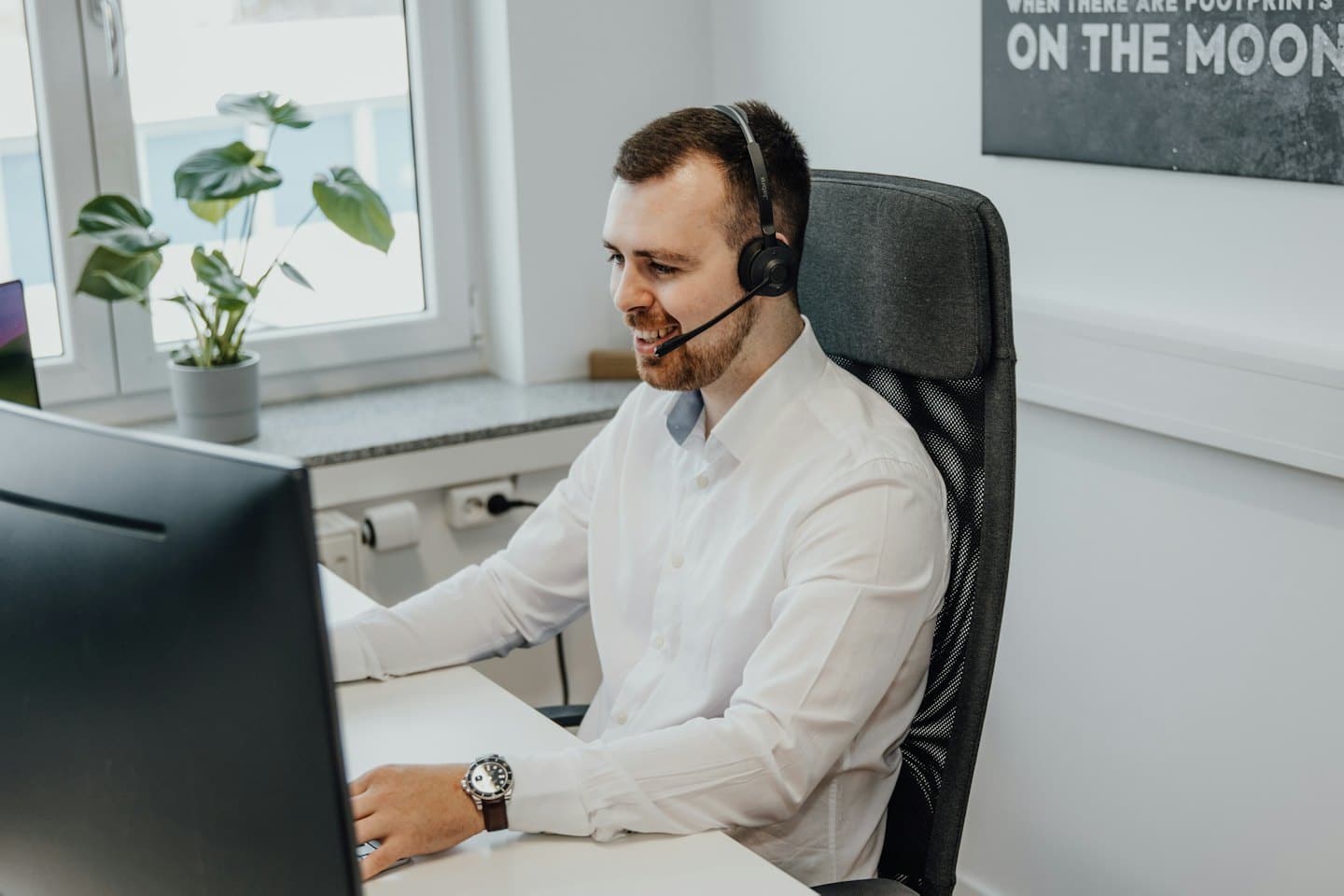 Ein Mann mit Headset lächelt, während er am Computer arbeitet.